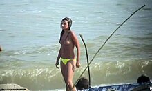 Uma bomba sem blusa mostrando seus seios empinados em uma praia de nudismo